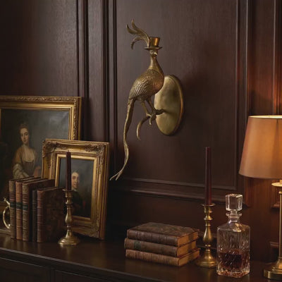 product video of an Emerson the Pheasant cast aluminum antique gold wall mount used as gold-wall-decor above candles, books, and a vintage globe